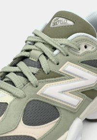 Baskets vertes et grises avec un dessus en maille et en daim, présentant un grand logo « N » blanc, des lacets texturés et une semelle rembourrée.