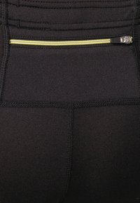Leggings sportivi neri con tasca posteriore con zip e accento giallo. Il tessuto è liscio e elastico con cuciture rinforzate.