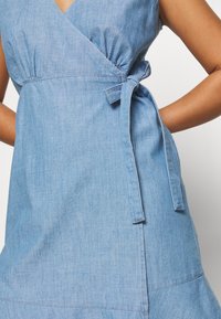 Jasnoniebieska sukienka typu chambray z krótkimi rękawami, zmarszczoną w talii i związanym paskiem. Miękka faktura i gładkie wykończenie.