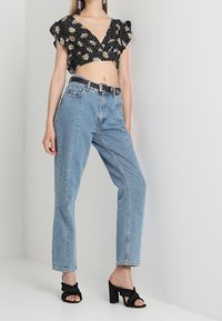 Top corto nero a fiori con maniche a volant, abbinato a jeans azzurri a vita alta e mule nere con tacco.