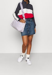 Sweat-shirt bicolore en bleu marine, rouge et blanc ; jupe en denim ; sac à épaule violet clair ; baskets blanches ; chaussettes en maille texturée.