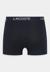Mornarske bombažne bokserice z širokim elastičnim pasom, na katerem je bel napis "LACOSTE". Gladka textura, oprijet dizajn, dolžina do sredine stegna.