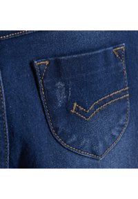 Blauwe denimstof toont een achterzak met gele stiksels en een V-vormige accent, met lichte vervaging en een gestructureerd oppervlak.