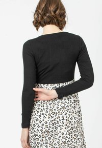Schwarzes, geripptes Langarmoberteil mit rundem Ausschnitt, kombiniert mit einem weißen Rock mit einem schwarz-orangen Blumenmuster.