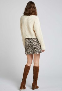 Un pull en crème tricoté épais, cropped, associé à une jupe mini à imprimé léopard et des bottes marron en suède hauteur genou avec des talons empilés.