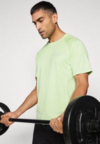 Light green athletic t-shirt with a crew neckline and raglan sleeves. The fabric appears smooth with a subtle texture. Logo printed on chest.