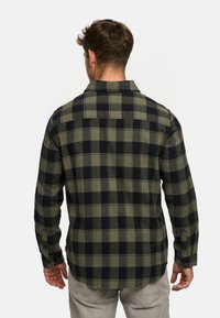 Camisa de franela a cuadros verdes y negros con mangas largas, cuello y puños abotonados, que presenta una tela texturizada y un dobladillo recto.