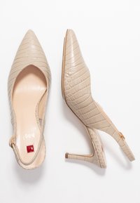 Escarpins beige à bout pointu et à talon slingback, avec une texture crocodile, des talons fins et une petite touche rouge sur la semelle intérieure.