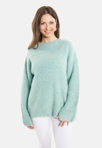 Hellgrüner, gestrickter Pullover mit lockerer Passform, weiten Ärmeln und subtiler Textur, kombiniert mit weißen Hosen. Geeignet für die Freizeit.