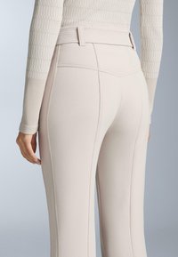 Jasne beżowe dopasowane spodnie z wysokim stanem, z poziomymi żebrowaniami na pasku oraz pionowymi przeszyciami po bokach.