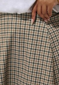 Beige rok met zwart en bruin houndstooth-patroon, met een zachte textuur en een lichte uitlopende zoom.