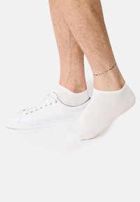 Hvide bomuldsankelsokker båret med hvide sneakers. Sokkerne har en glat tekstur og en ribbet kant, som giver en tætsiddende pasform.