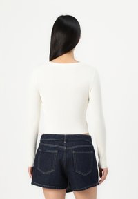 Top bianco a maniche lunghe con righe abbinato a pantaloni denim scuri. I pantaloni presentano un classico design a cinque tasche e una vita standard.