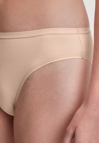 Beige Stoffunterhose mit glatter Textur, mid-rise Design und elastischem Bund, auf Haut präsentiert.