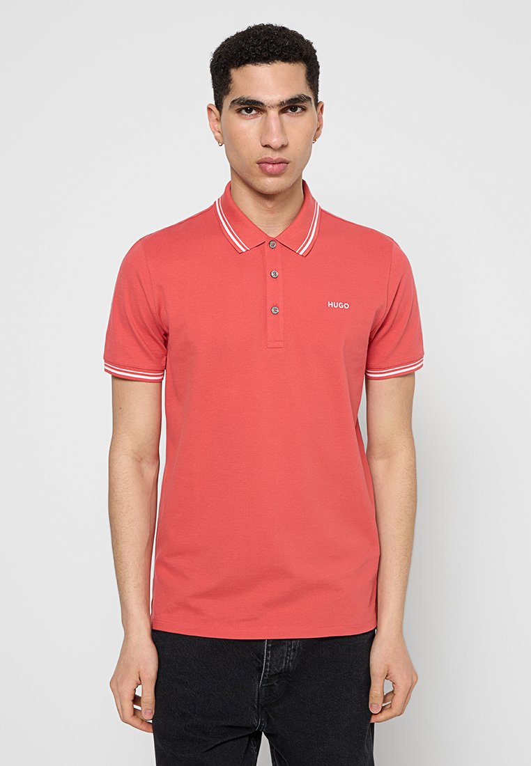 Czerwona koszulka polo z białymi paskami przy kołnierzyku i krótkimi rękawami, z trzema guzikami i małym logo na klatce piersiowej. Gładka bawełniana tekstura.