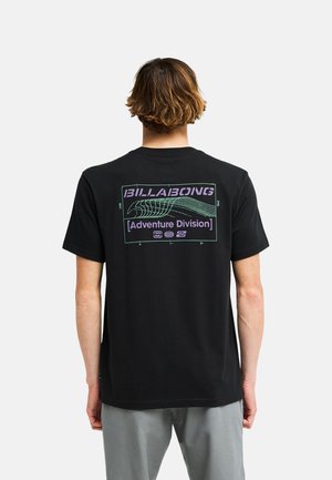 Persona con capelli corti castani vista da dietro che indossa una maglietta nera Billabong con una grafica di onda viola e verde e testo "Adventure Division."