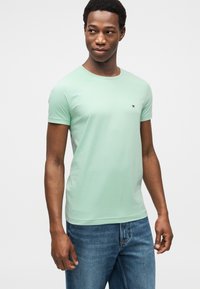 Ανοιχτό πράσινο βαμβακερό T-shirt με στρογγυλή λαιμόκοψη και κοντά μανίκια. Διαθέτει μικρό λογότυπο στο στήθος. Φορεμένο με μπλε τζιν παντελόνι.