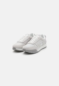 Lysegrå atletik-sneaker med en glat og tekstureret finish. Har snørebånd foran, polstret krave og logo på siden. Gummisål.