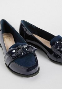 Ballerine blu navy con finitura in pelle verniciata lucida, caratterizzate da una fascia in suede e un fiocco decorativo sulla punta.