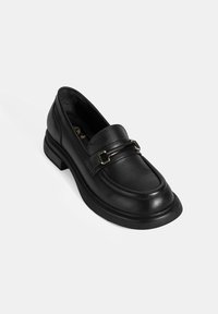 Schwarze Lederloafer mit runder Zehenpartie, einer gestickten Akzentuierung entlang der Kante und einem Metallriemen-Detail über dem Vorderschuh. Niedriger, stabiler Absatz.