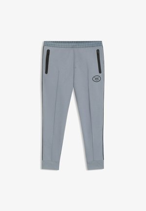 Pantaloni sportivi grigi con tasche con zip nere, vita elasticizzata, gambe affusolate e un'etichetta con logo. Texture liscia con dettagli di design sottili.