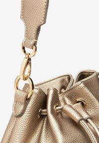 Guldmetallisk læderhåndtaske med en tekstureret overflade, der har en guldhardware-holder og snorelukning med forstærkede øjer.