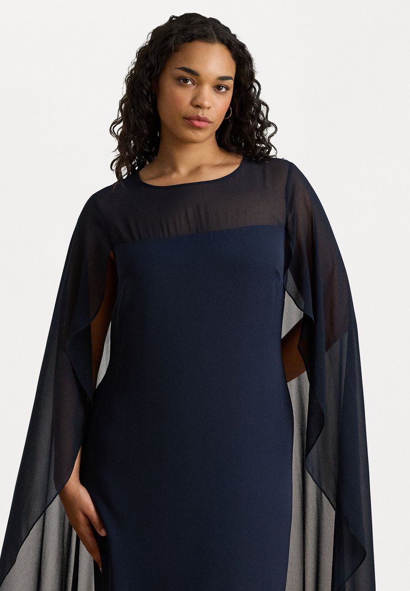 Abito blu navy fluente con maniche a capesce trasparenti, tessuto morbido, scollo rotondo e drappeggio sottile. Presenta una silhouette aderente e fessure laterali.