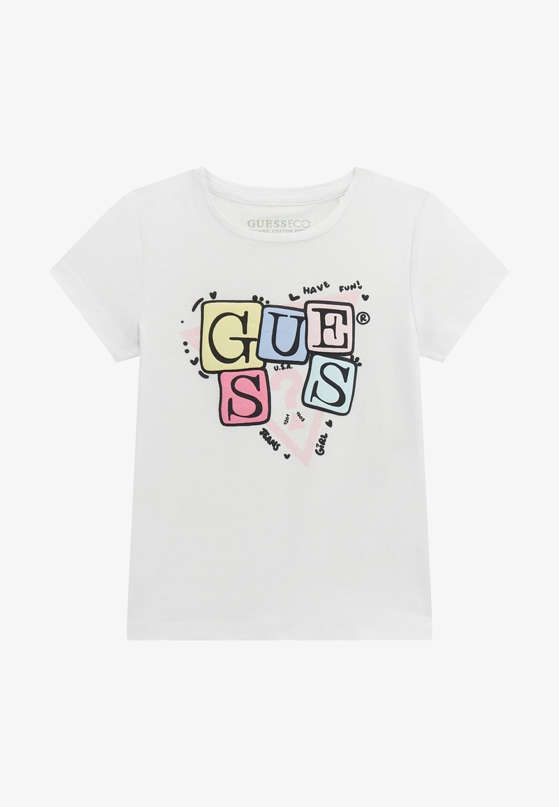 Valge lühikeste varrukatega T-särk, mis on valmistatud orgaanilisest puuvillast, sisaldab värvilist plokk-tähtedega "GUESS" graafikat koos jooniste ja mänguliste tekstielementidega.