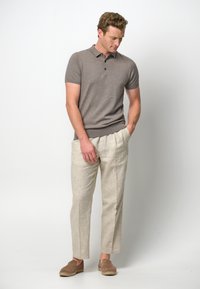 Brun kortärmad polo med tre knappar, kombinerad med ljusbeiga linbyxor och bruna slip-on skor. Enkel, avslappnad passform.