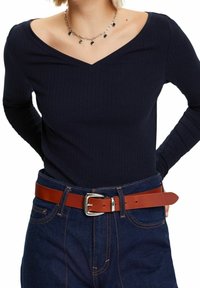 Laivastonsininen raidoitettu pitkähihainen paita, jossa on V-kaula-aukko, yhdistettynä korkeavyötäröisiin sinisiin farkkuihin ja ruskeaan nahkavyöhön, jossa on hopea solki.