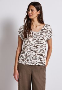 Maglietta a maniche corte color crema con stampa zebra marrone, caratterizzata da un fit rilassato e scollatura a girocollo, abbinata a pantaloni larghi marroni.