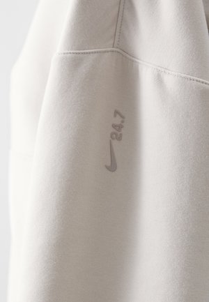 Hellgrauer Sweatshirt aus weichem Material, mit einem Nike-Logo und der Aufschrift "24.7" in einem etwas dunkleren Farbton. Glatte Textur, minimalistisches Design.