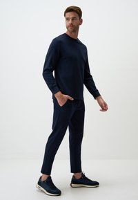 Dunkelblauer Langarm-Sweatshirt und schmal geschnittene Hose aus weichem Material. Die Hose verfügt über seitliche Taschen und wird mit navyblauen Sportschuhen kombiniert.