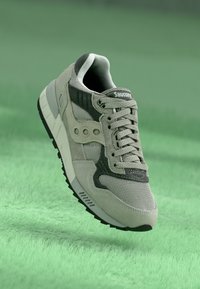 Baskets grises en matériaux en maille et en daim, dotées d'un accent noir, d'une semelle texturée et d'un design à lacets. Logo visible sur la languette.