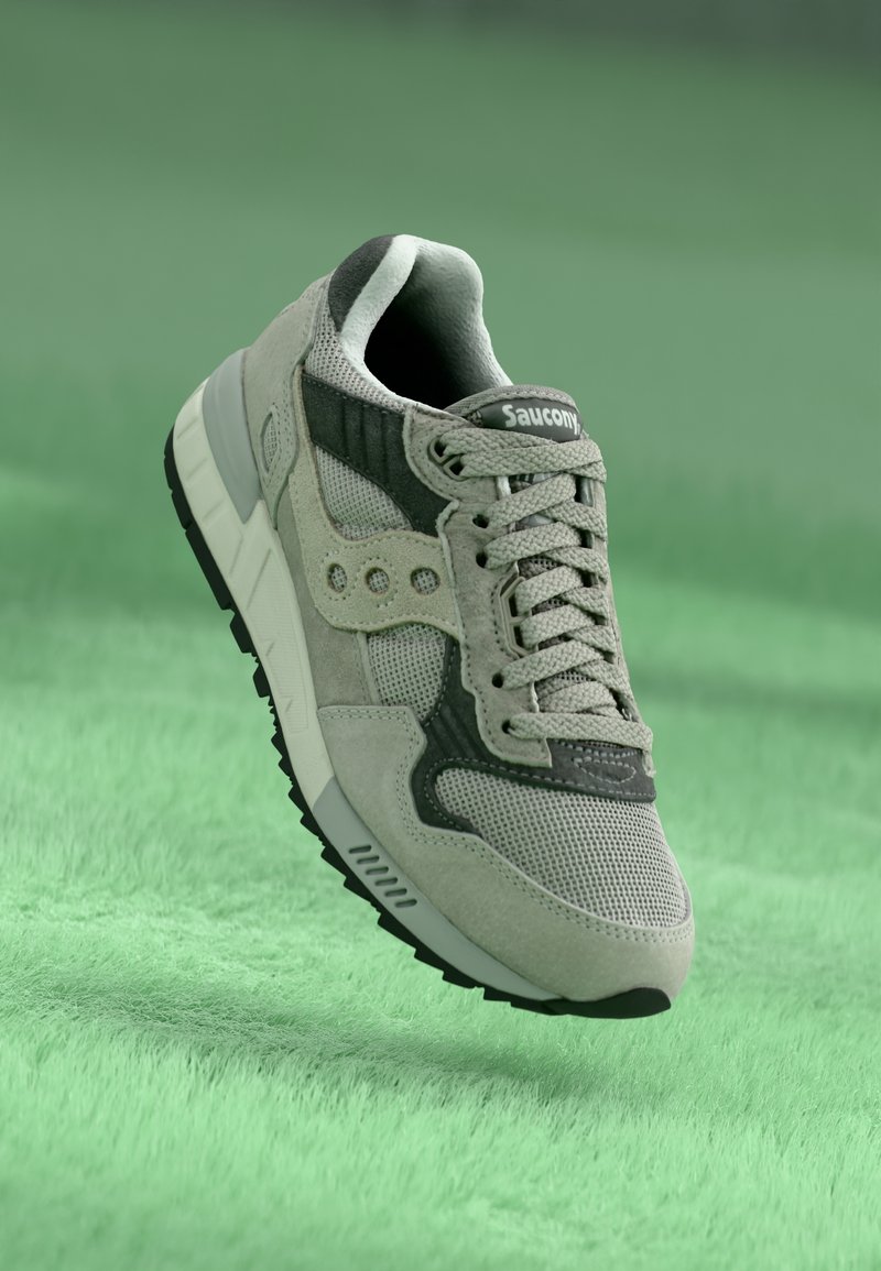 Baskets grises en matériaux en maille et en daim, dotées d'un accent noir, d'une semelle texturée et d'un design à lacets. Logo visible sur la languette.