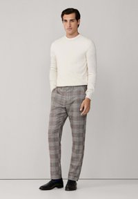 Cremfarbener Pullover mit langen Ärmeln, kombiniert mit grauen Karohosen. Schwarze Schuhe vervollständigen das Outfit. Einfaches, maßgeschneidertes Design.