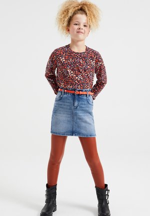 Blomstret langærmet top i rød og blå, parret med en blå denimnederdel og brune blanke leggins. Sorte ankelstøvler med spænder fuldender outfittet.