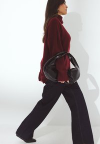 Schwarze Lederhandtasche mit runder Form, kombiniert mit einem lockeren burgunderfarbenen Pullover und dunklen, weiten Jeans, die einen lässigen Look kreieren.
