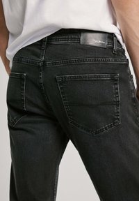 Mustat farkut slim fit -leikkauksella, joissa on takataskut ja nahkainen merkkilappu vyötäröllä. Sileä tekstuuri ja siisti ompelu.