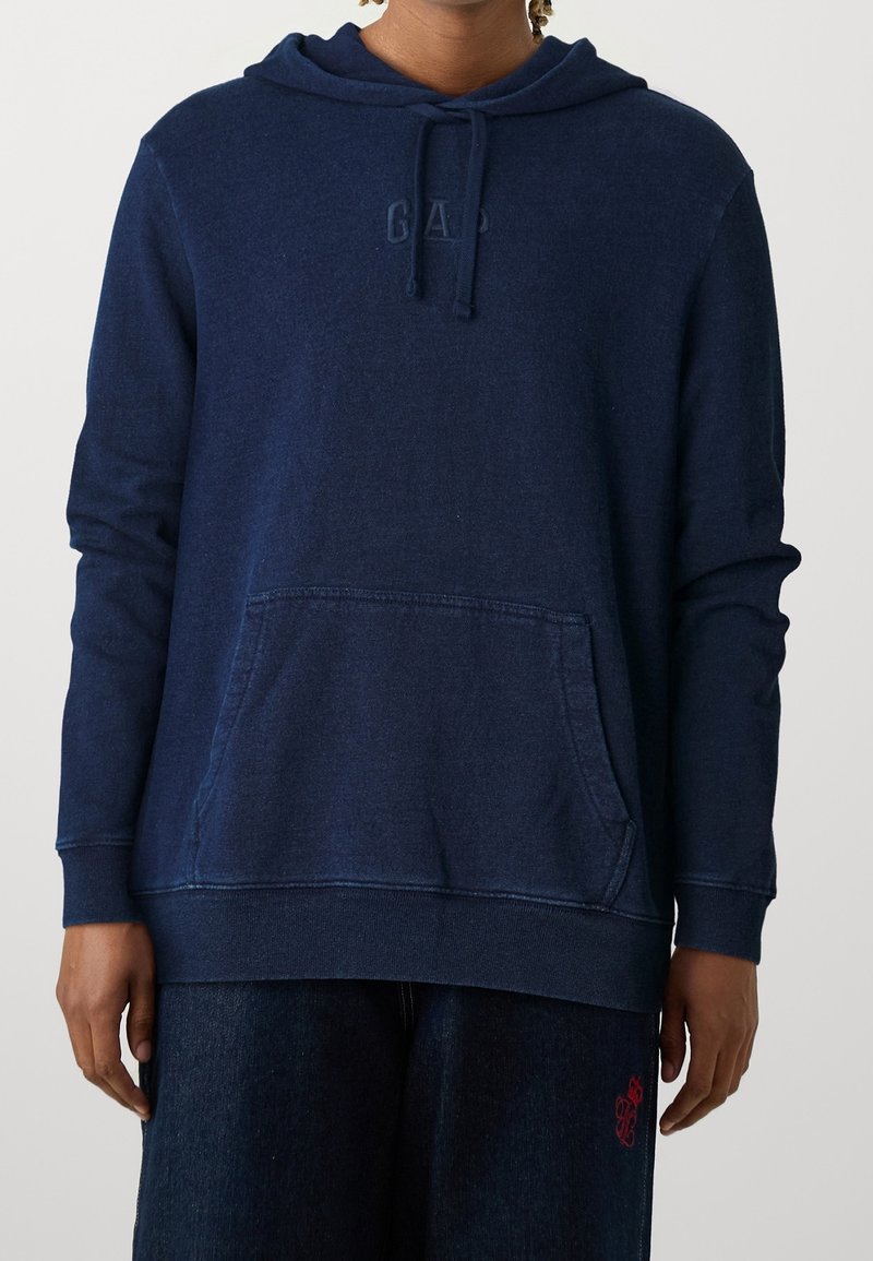 Felpa blu navy realizzata in tessuto morbido, con tasca frontale, cappuccio con lacci e logo "GAP" in rilievo sul petto. Vestibilità comoda.