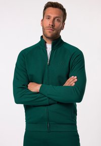Giacca verde con zip e colletto alto, realizzata in tessuto morbido. Presenta una cerniera frontale e un dettaglio con logo, con polsini e orlo a costine.