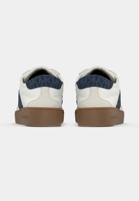 Baskets blanches avec un arrière bleu marine à motif, présentant un matériau texturé, des semelles en caoutchouc et des détails de couture.