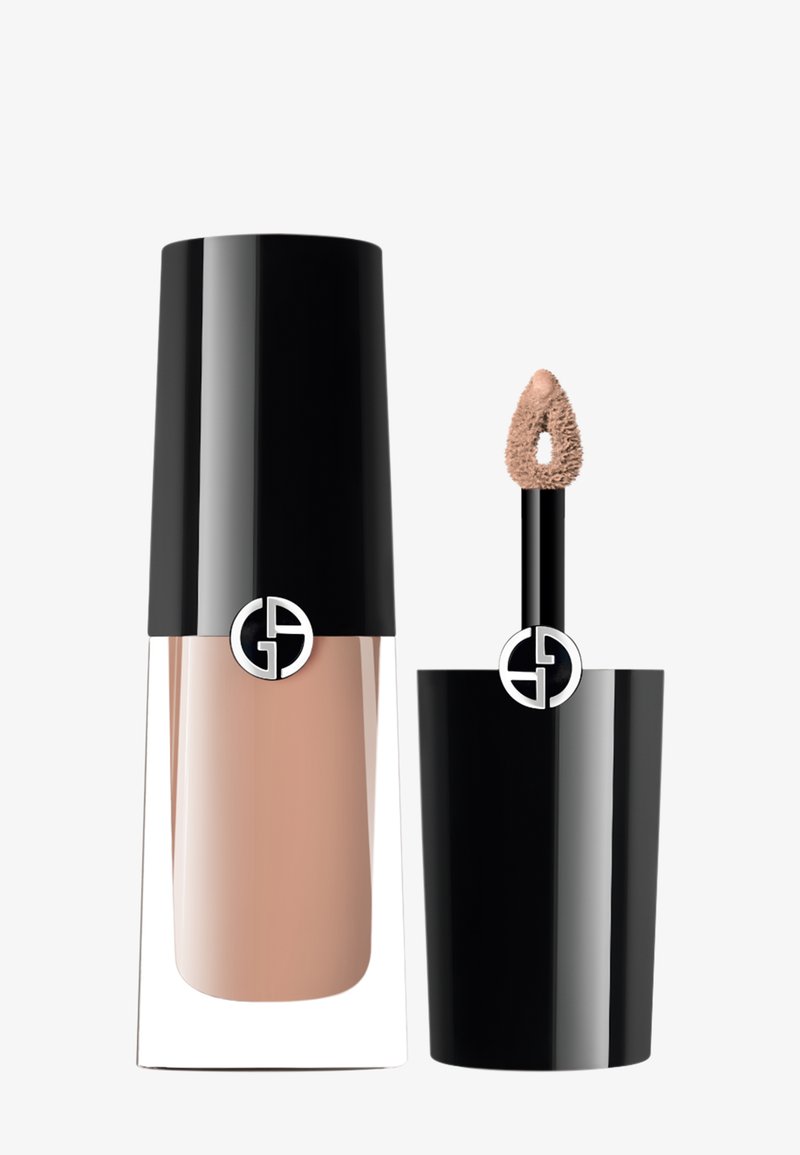 Flytende foundation i en klar glassflaske med svart lokk; inkluderer en applikator med en myk tupp. Lys beige nyanse.