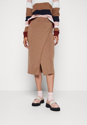 Person iført en brun wrap-style midi-nederdel, flerfarvet stribet sweater, lyserøde sokker og chunky beige loafers med regnbuestrimler.
