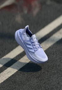 Vit Adidas löparsko med Boost-sula som svävar över asfaltväg med vit linje i bakgrunden.