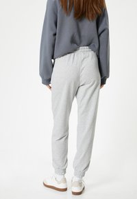 Pantaloni grigi in felpa con vita elastica e polsini, realizzati in un tessuto morbido. Abbinati a sneakers bianche con un accento beige.