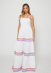 Abito maxi bianco con corpetto arricciato, gonna a strati e decorazioni a zigzag colorate in blu, rosa e arancione lungo l'orlo e le spalline.