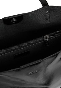 Interior de un bolso de mano de cuero negro que muestra un bolsillo con cremallera, cierre a presión y forro de tela texturizada con detalle del logo en relieve "W.11".