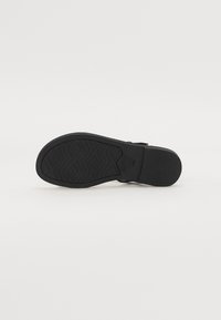 Suela de zapato negra con un patrón de agarre texturizado, presenta un borde liso y una leve curvatura en el tacón. Fabricada en material de goma, diseño plano.