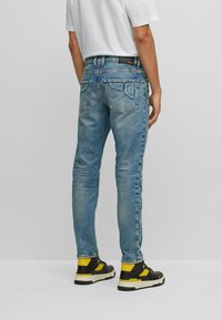 Ljusblå denimjeans med slim fit, femficksdesign och distinkt sömnad på bakfickorna. Bärs med svarta och gula sneakers.